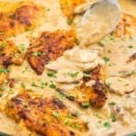 Chicken stroganoff in a cast iron pan. A spoon is adding sauce over a cutlet.