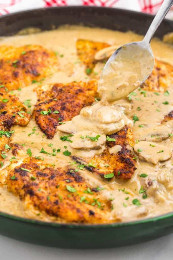Chicken stroganoff in a cast iron pan. A spoon is adding sauce over a cutlet.