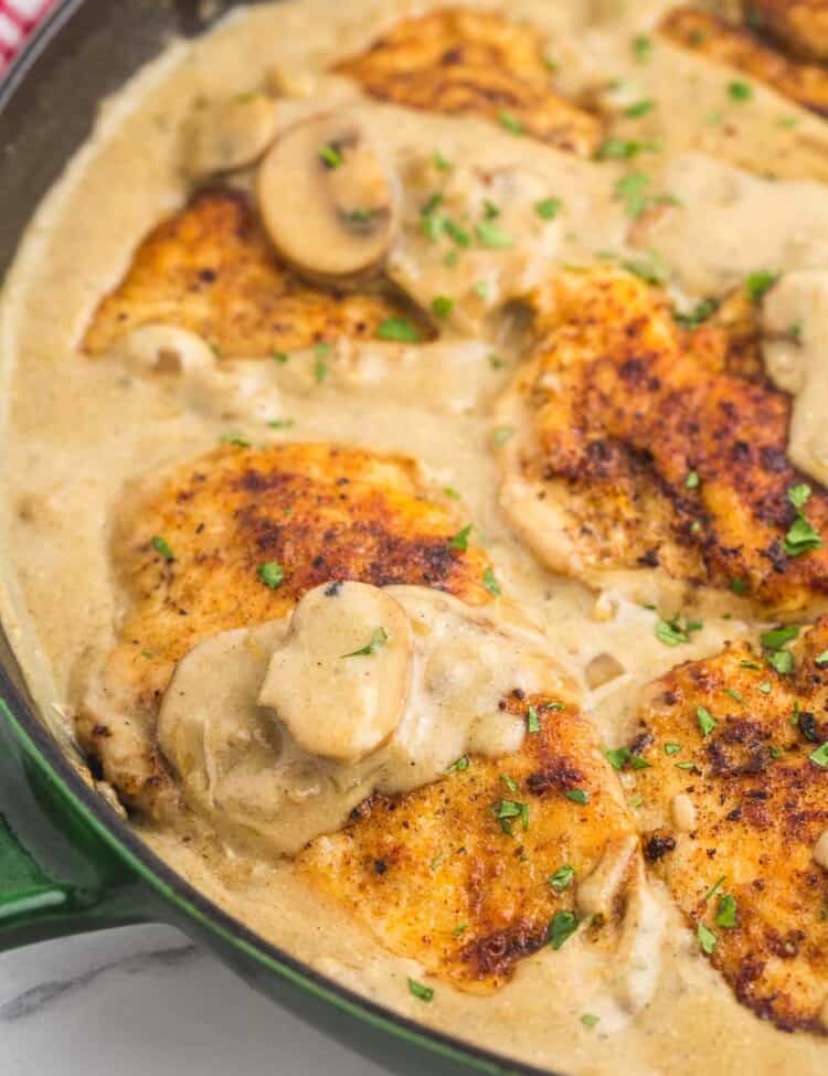 half of a cast iron pan filled with creamy sauce and chicken cutlets with mushrooms