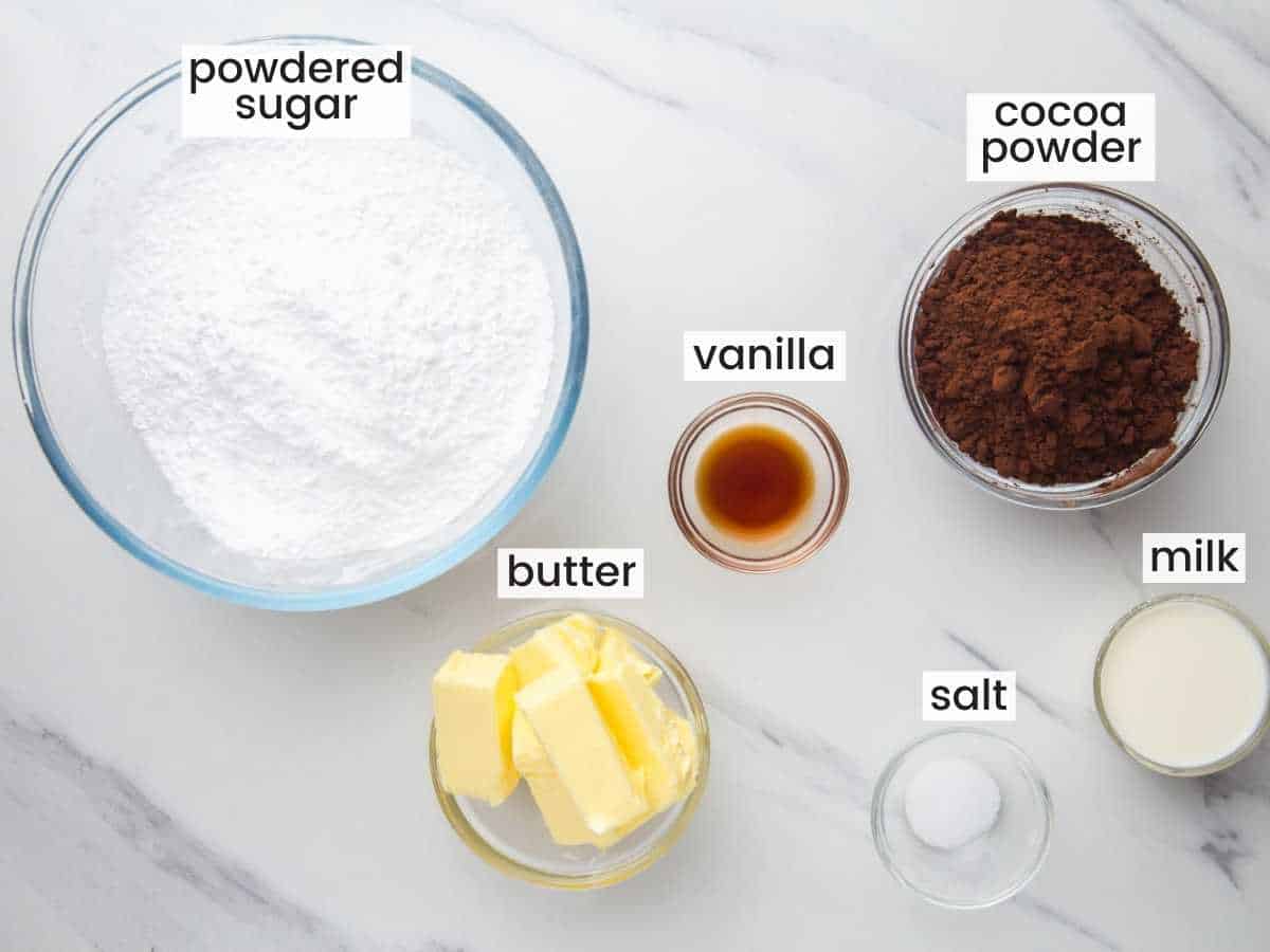 The ingredients for chocolate buttercream in separate glass bowls on a marble counter