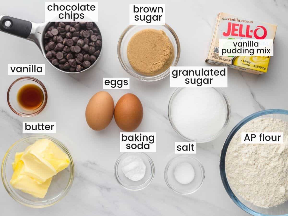 The ingredients needed to make chocolate chip pudding cookies, in separate bowls on a marble counter top