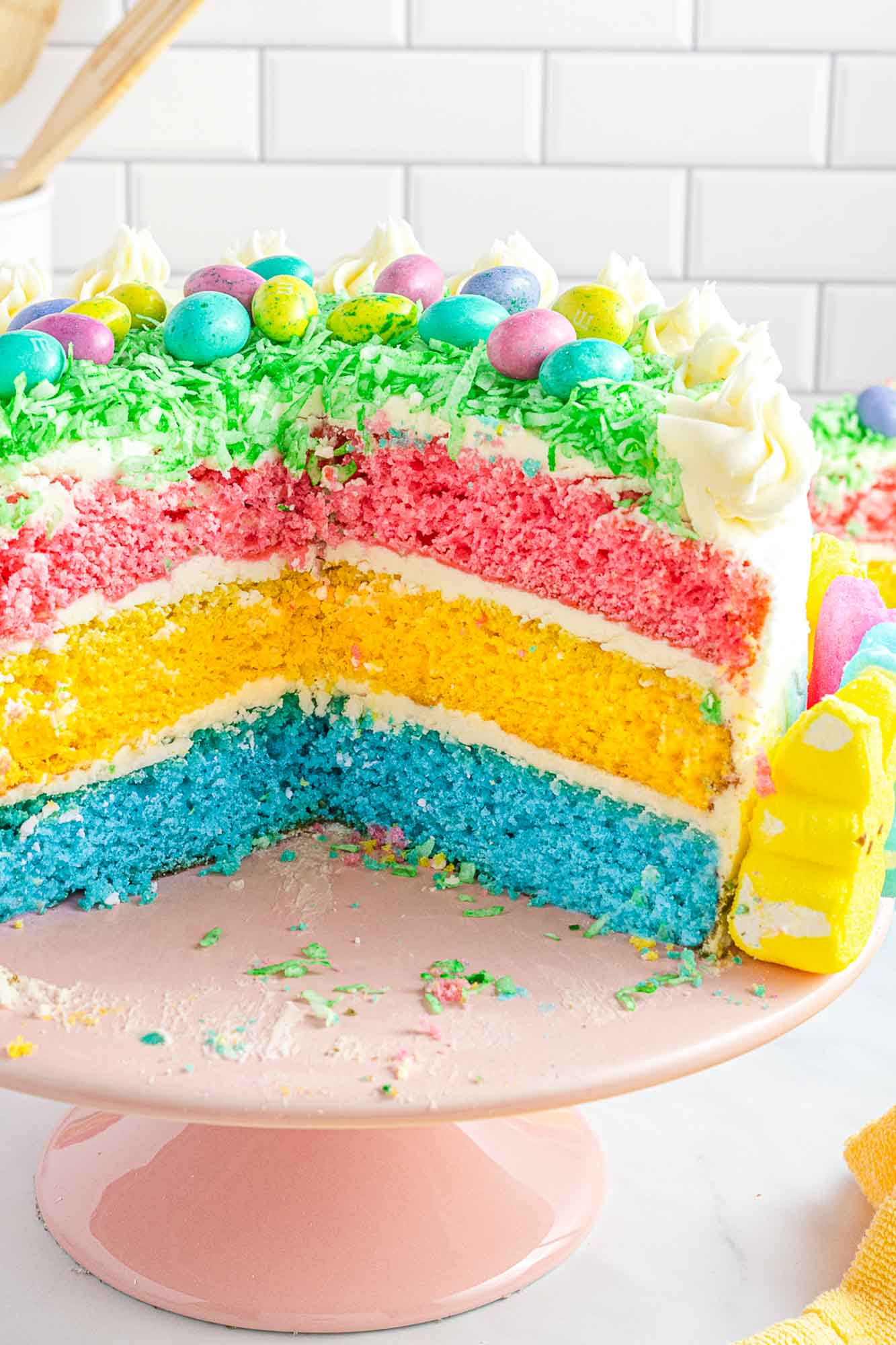 Easter layer cake with 3 different layers: pink, yellow, and blue. Shown on a pink cake stand.