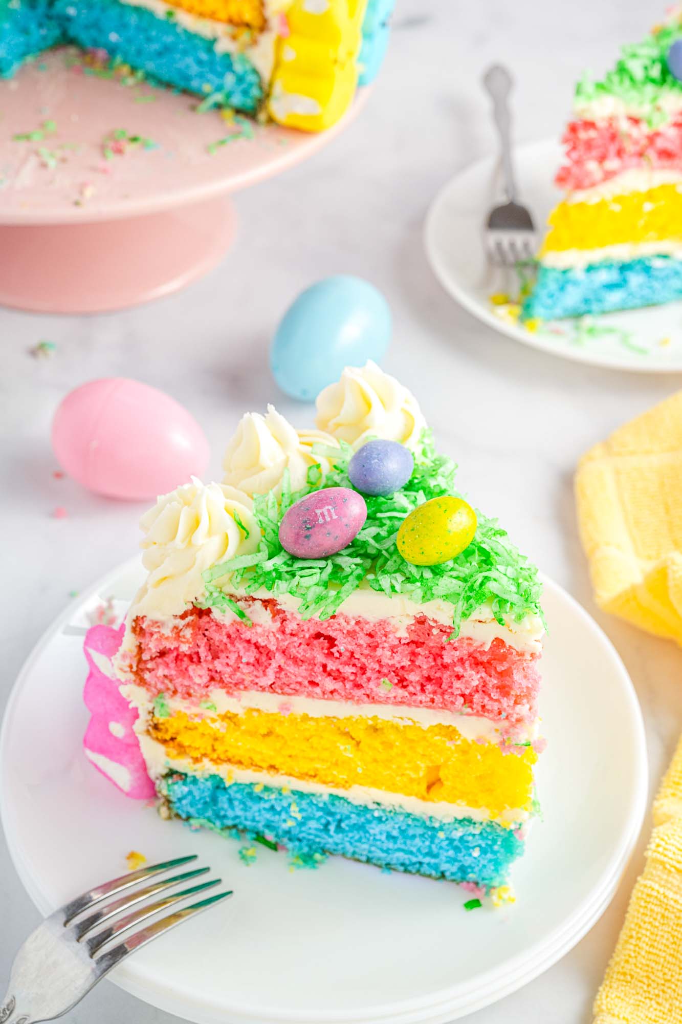 A slice of colorful layer cake with easter decorations served on a white plate with a fork