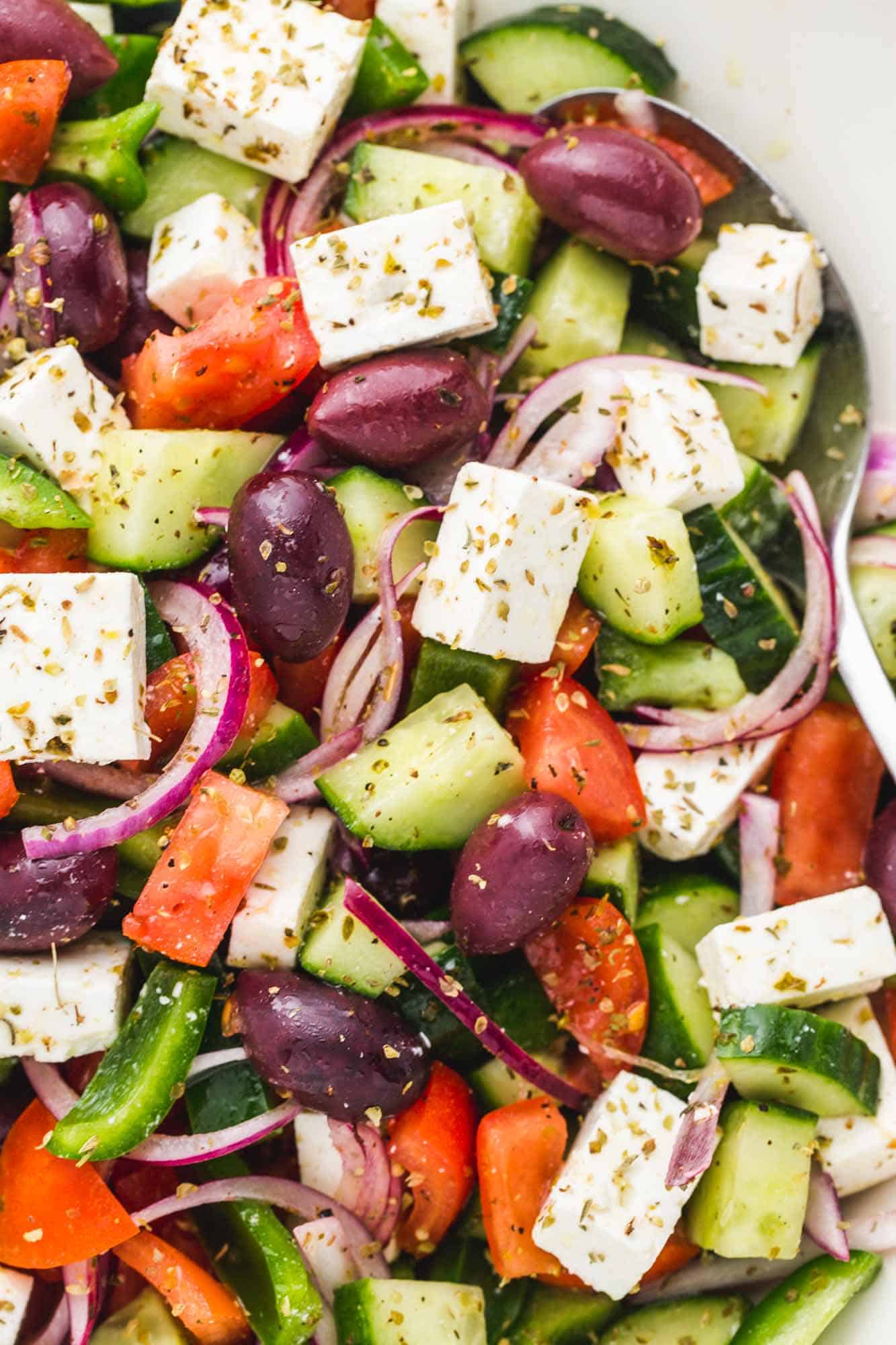 chopped greek salad with large pieces of cucumbers, onions, tomatoes, olives, and feta cheese cubes.