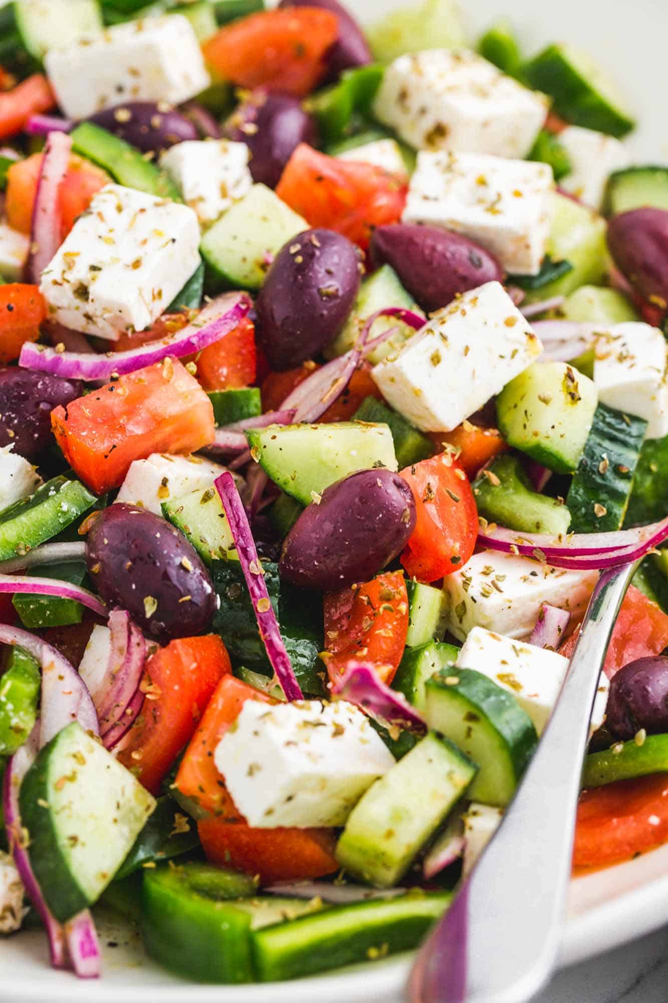 closeup view of a chopped green salad with feta, olives, cucumbers, peppers, and onions