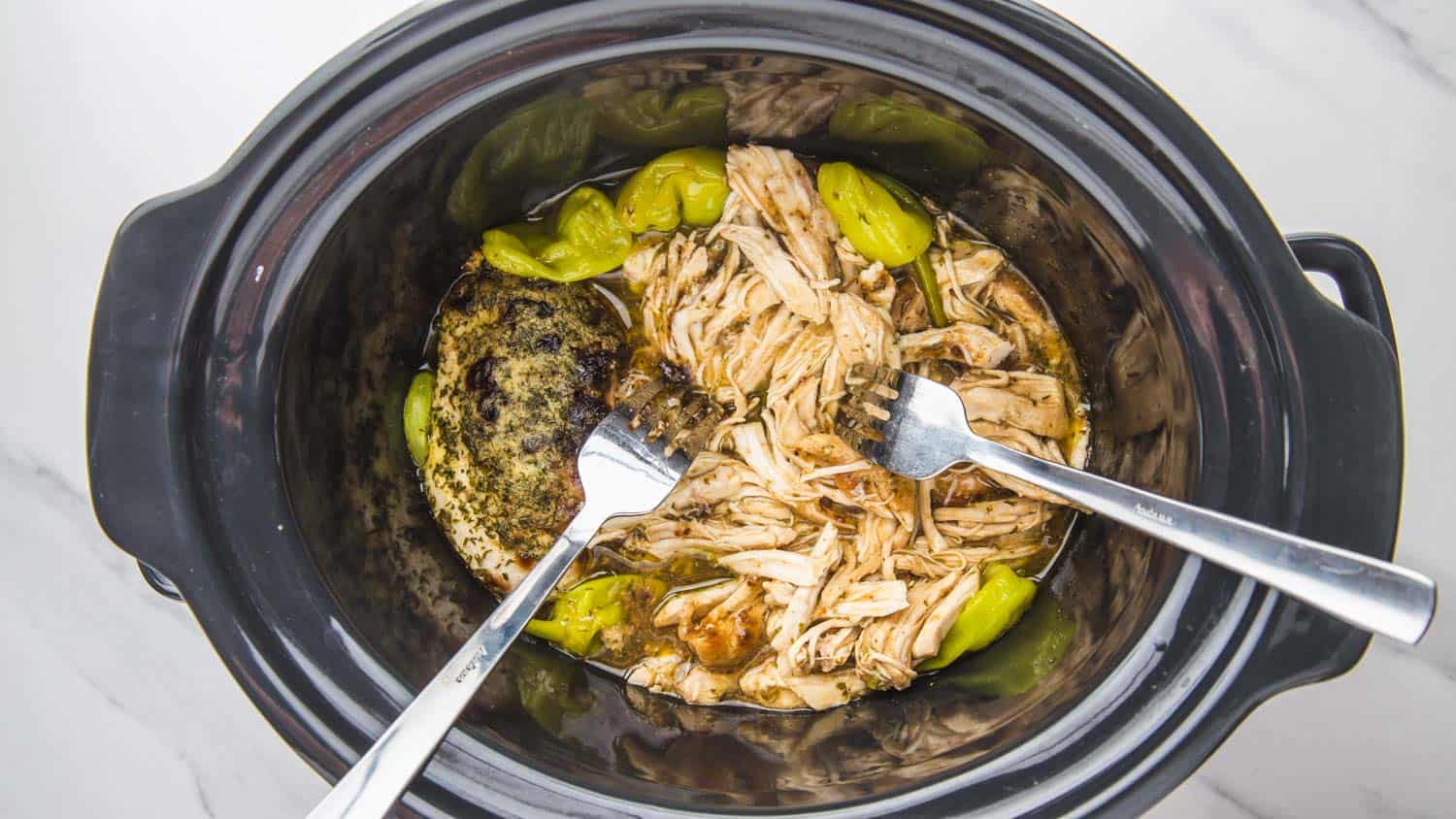 two forks being used to shred mississippi chicken in a crock pot insert