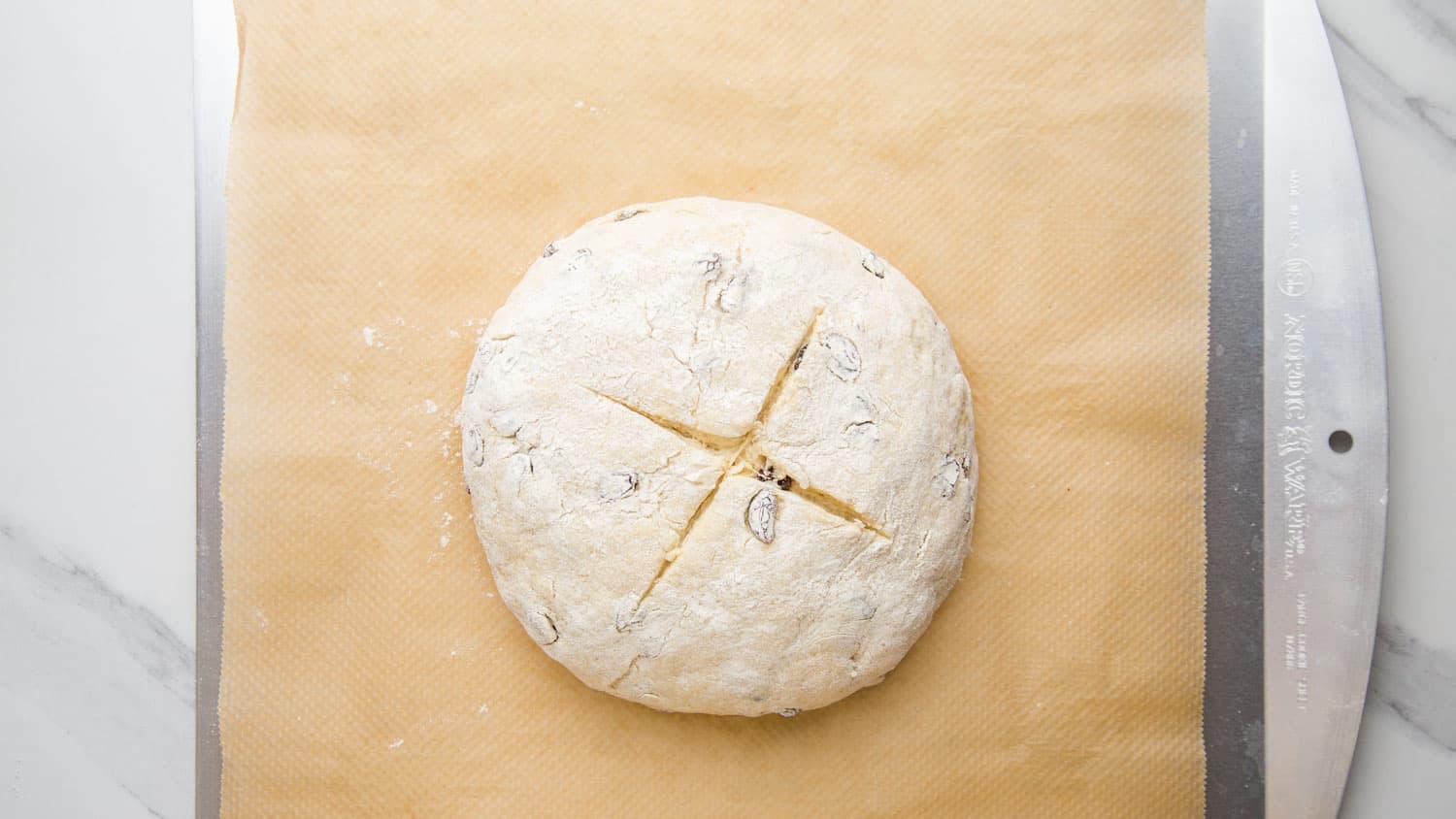 Shaped and scored irish soda bread dough ball placed on a baking sheet