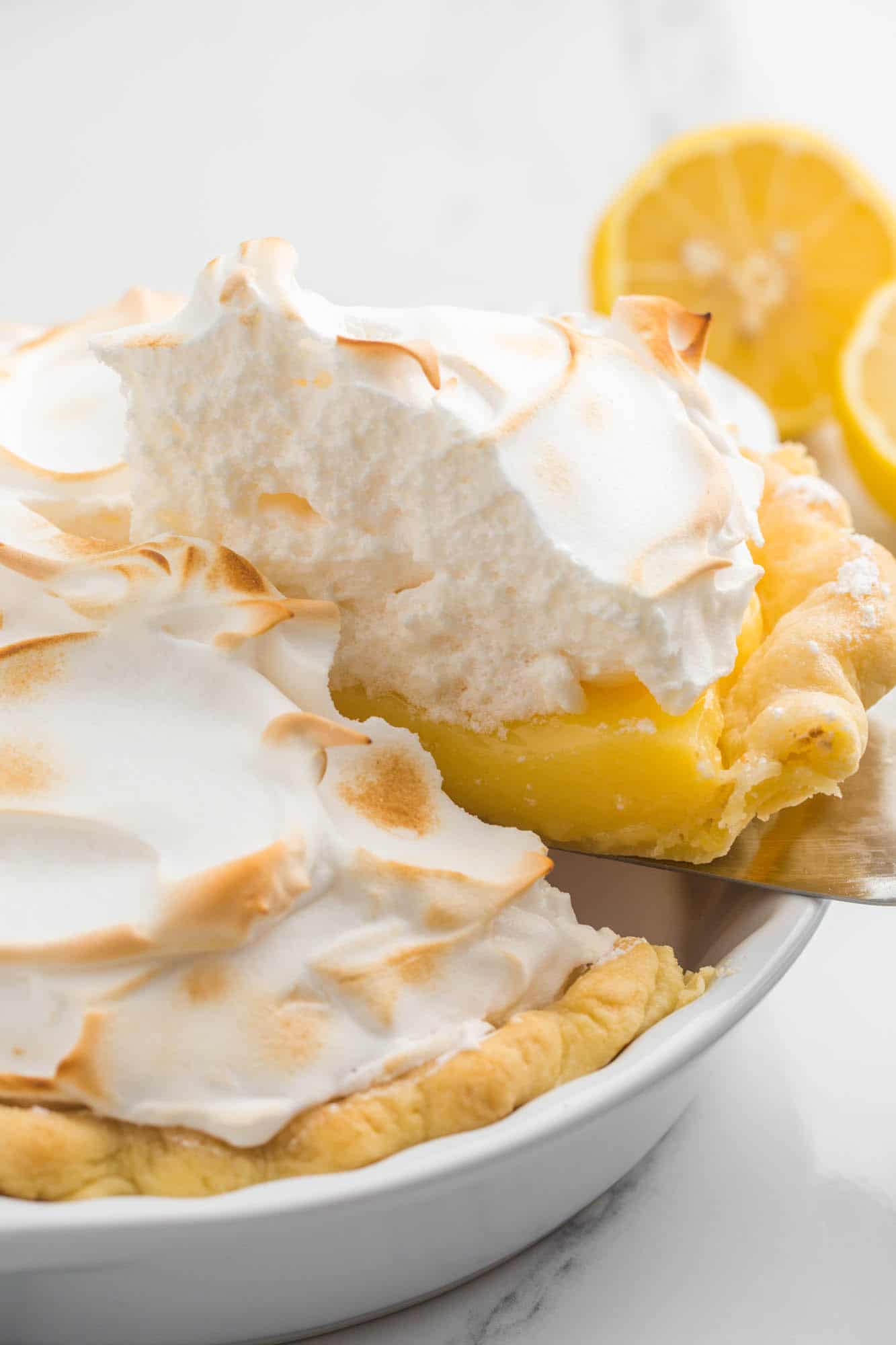 a homemade lemon pie with toasted meringue topping. A slice is being lifted out of the pan.