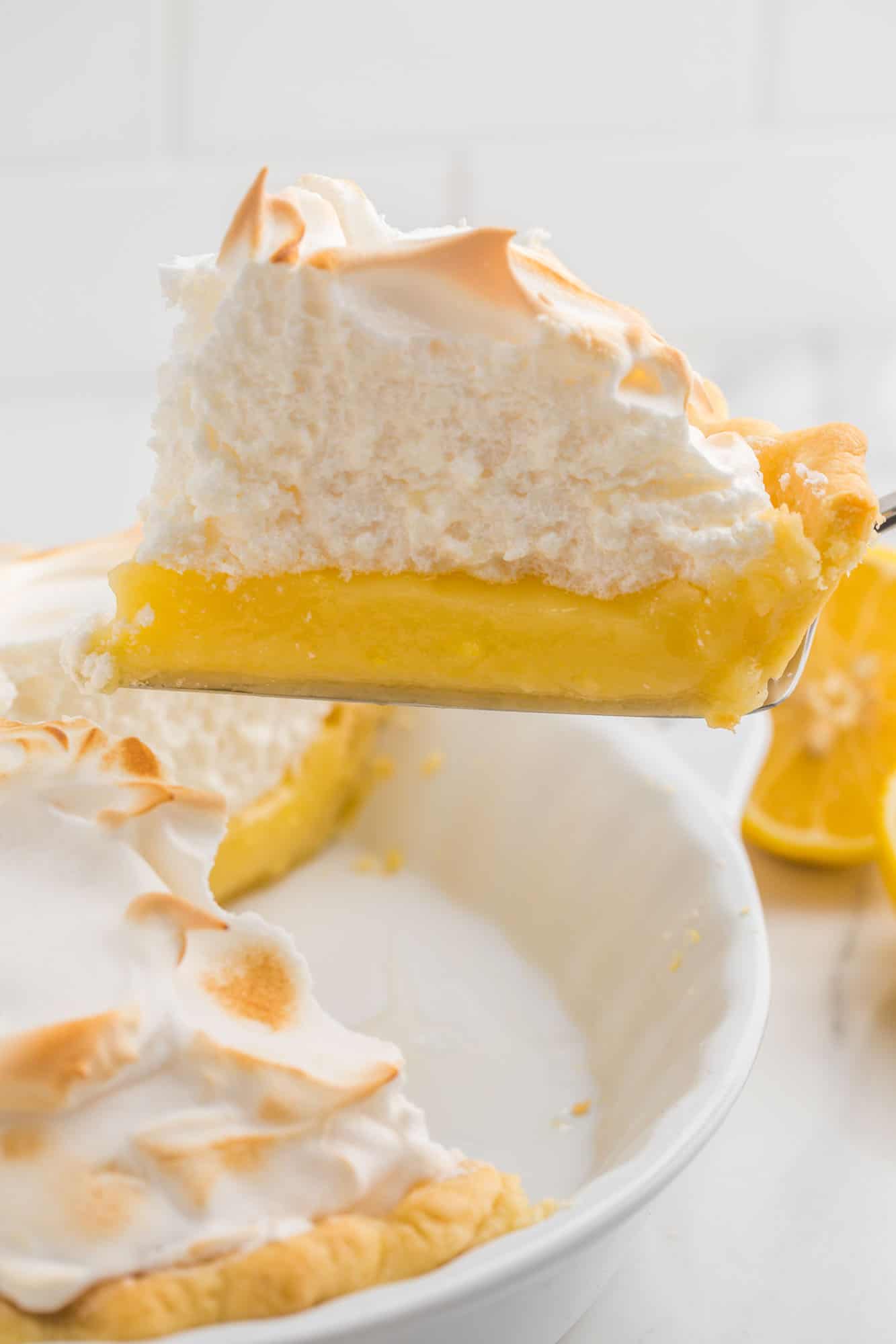 a slice of lemon meringue pie with a thick, fluffy meringue layer being lifted out of a white ceramic pie plate