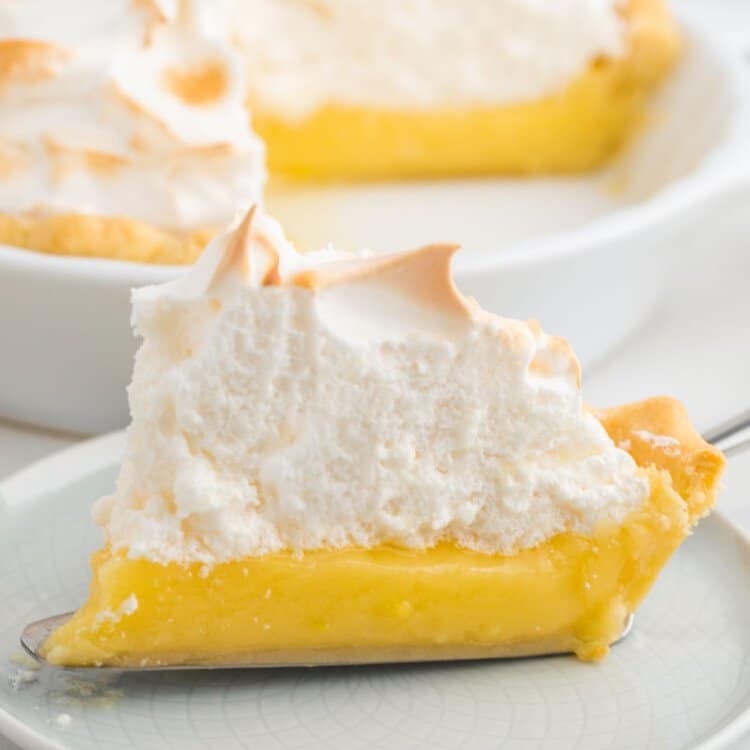 a slice of lemon meringue pie with a thick layer of fluffy meringue on a white plate.