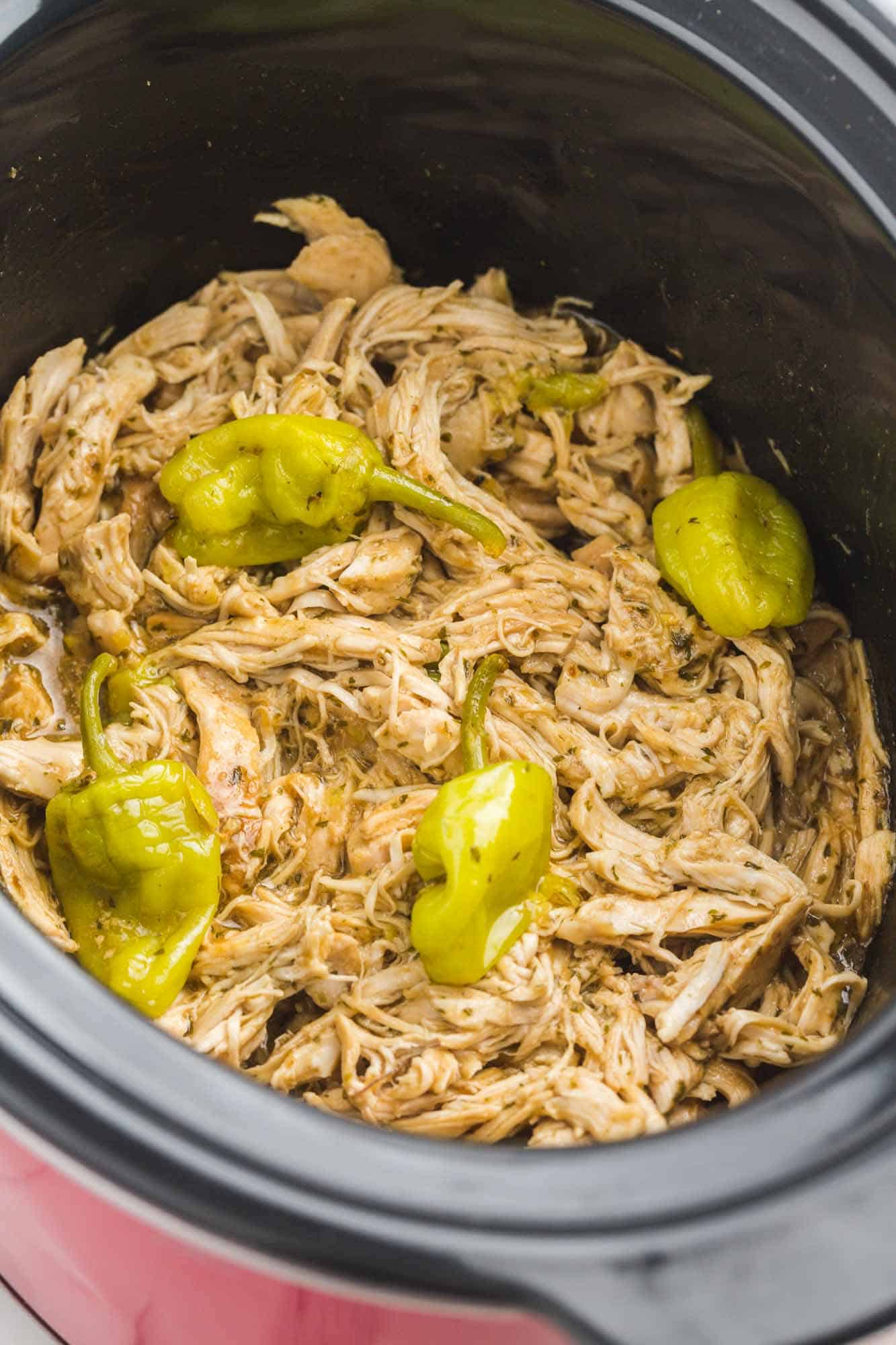 shredded mississippi chicken and pepperoncini in a black slow cooker.