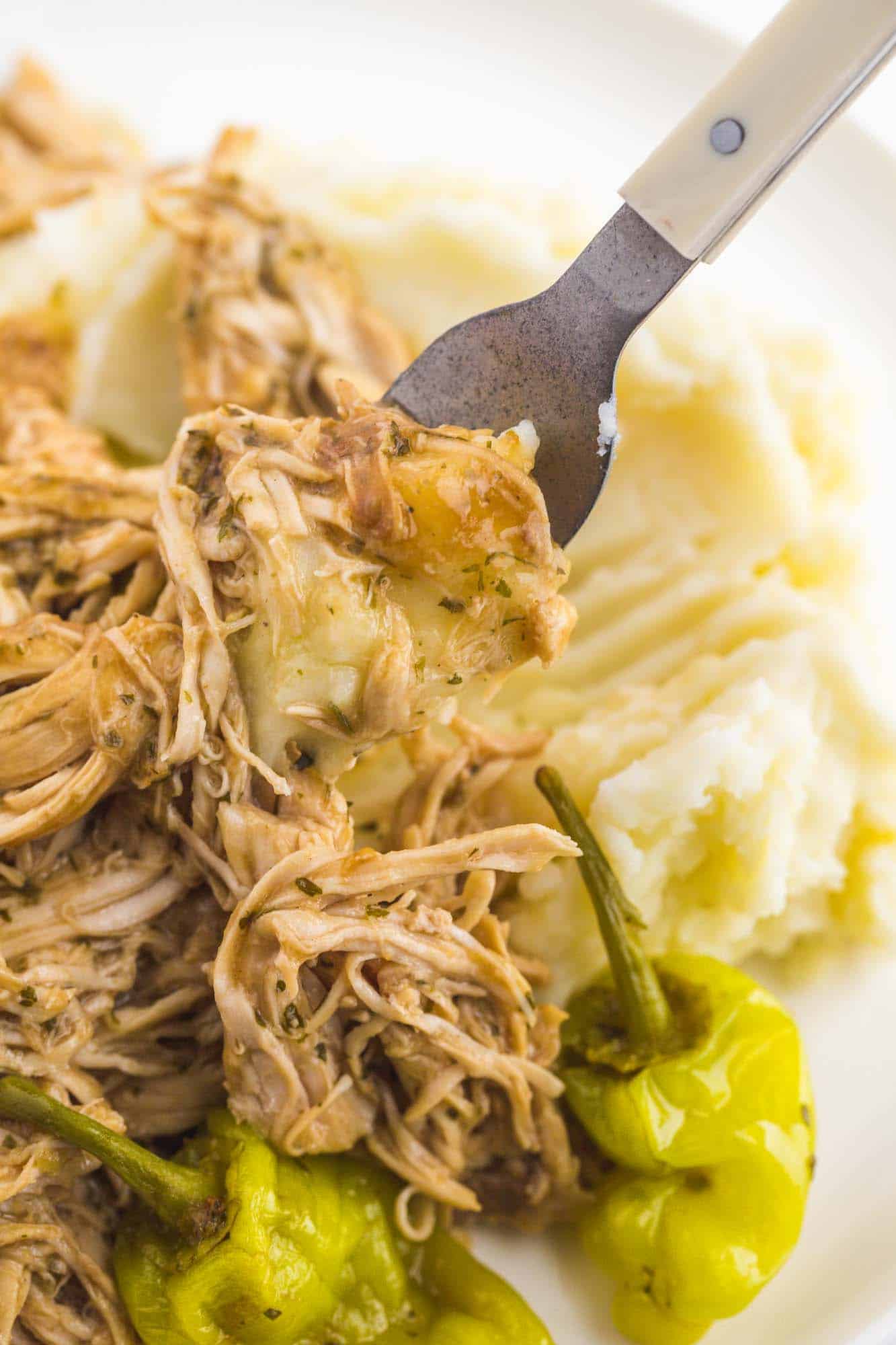 closeup view of a fork picking up a bite of shredded mississippi chicken from a plate of mashed potatoes