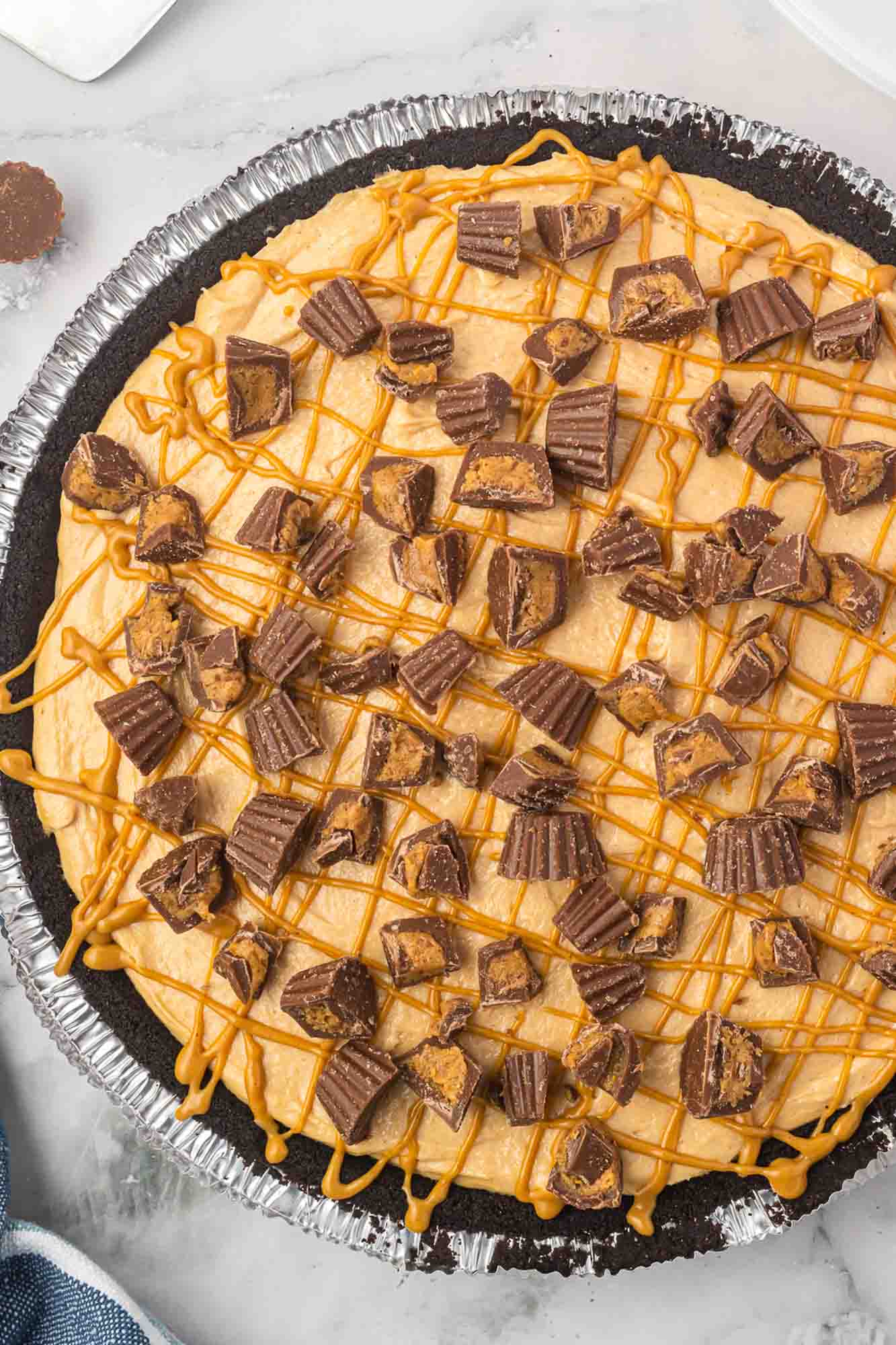 a full no bake peanut butter pie made in a premade chocolate graham cracker crust. The pie is drizzled with peanut butter and covered with mini reese's cups.