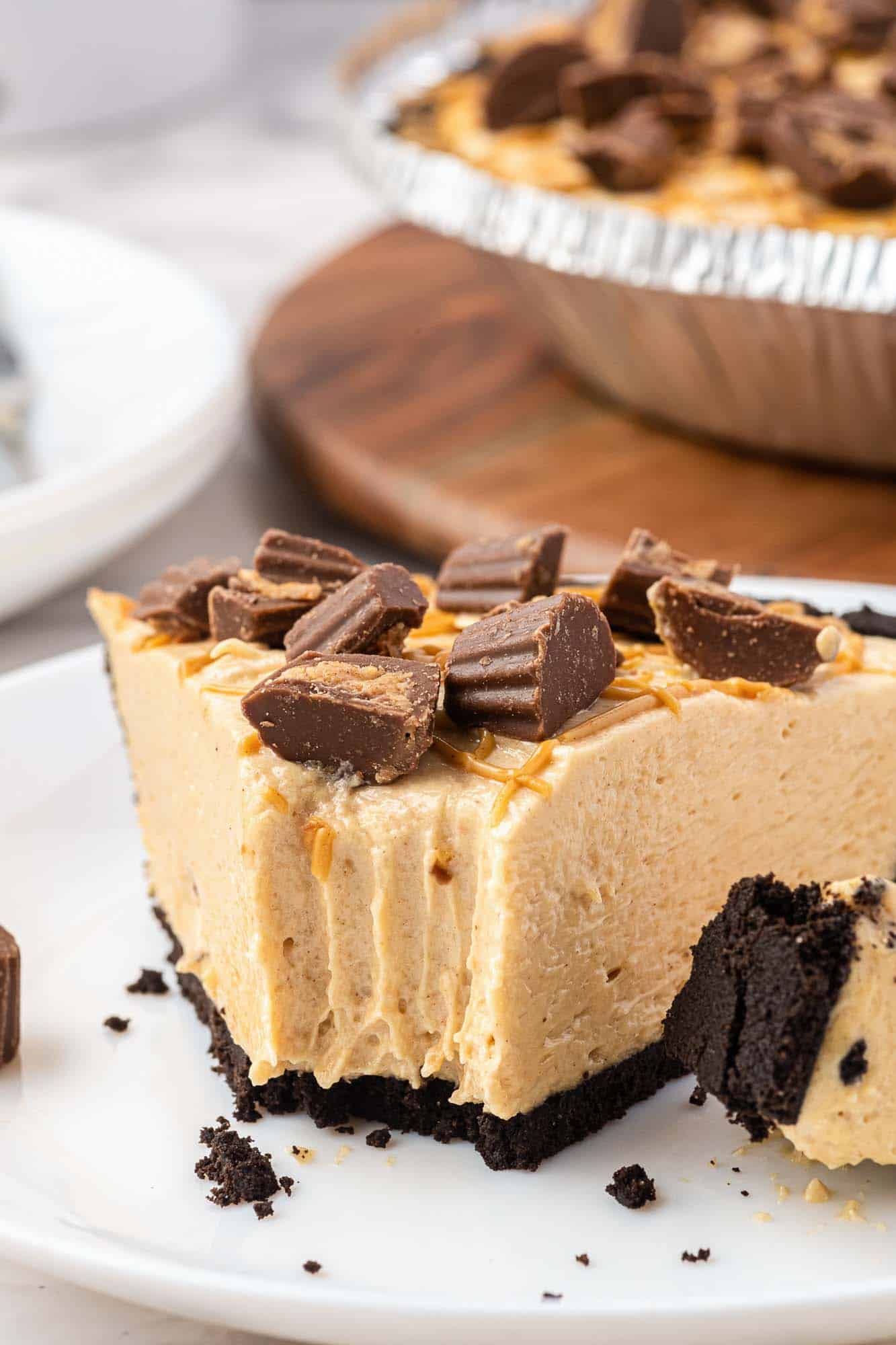 a single slice of no bake peanut butter pie is on a plate. A bite has been taken from the front of the pie. 