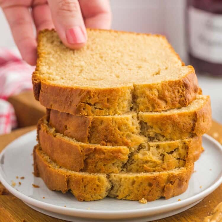 Peanut butter bread slices stacked on a small plate, and a hand taking a slice.