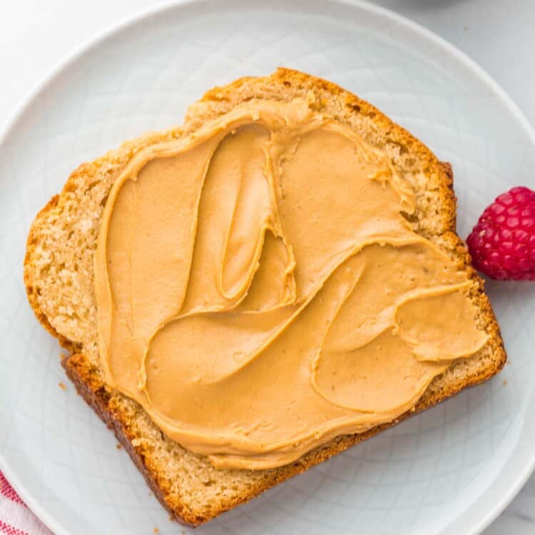 Overhead shot of a slice of peanut butter bread with smooth and creamy peanut butter spread on it, and a raspberry on the side.