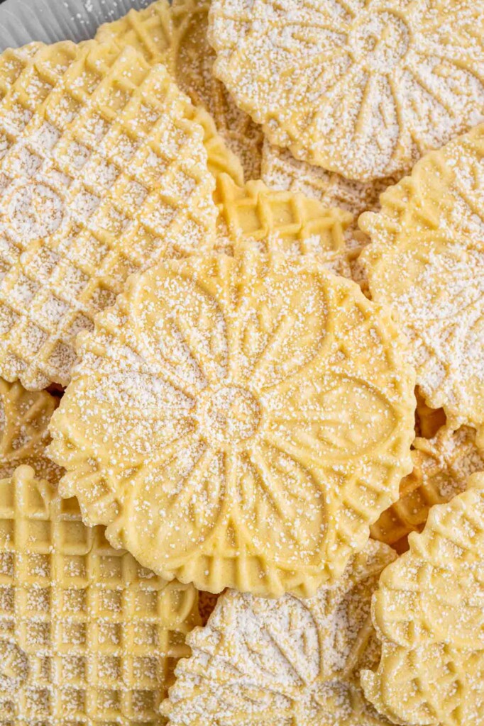Closeup view of a pile of pizzelles, some with flowers and some with waffle patterns