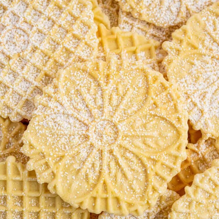 Closeup view of a pile of pizzelles, some with flowers and some with waffle patterns