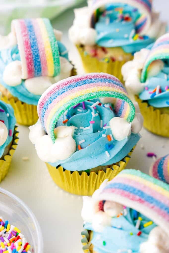 Rainbow cupcakes decorated with blue buttercream and rainbow stip candy and sprinkles