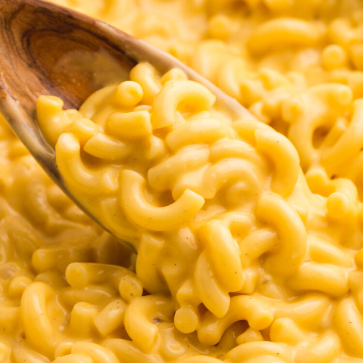 closeup view of a pot of homemade creamy elbow mac and cheese stirred with a wooden spoon