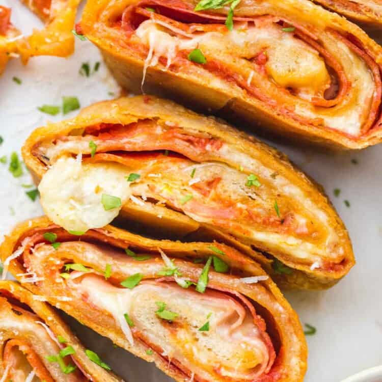 slices of stromboli filled with cheese and pepperoni on a plate, garnished with parsley and with a side of marinara sauce.