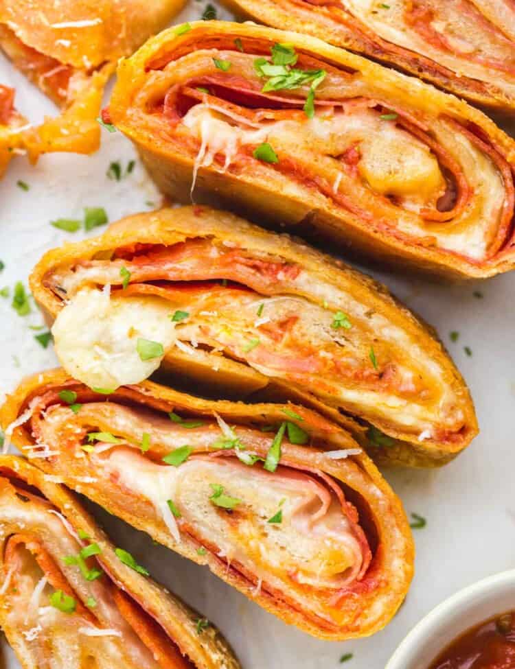 slices of stromboli filled with cheese and pepperoni on a plate, garnished with parsley and with a side of marinara sauce.