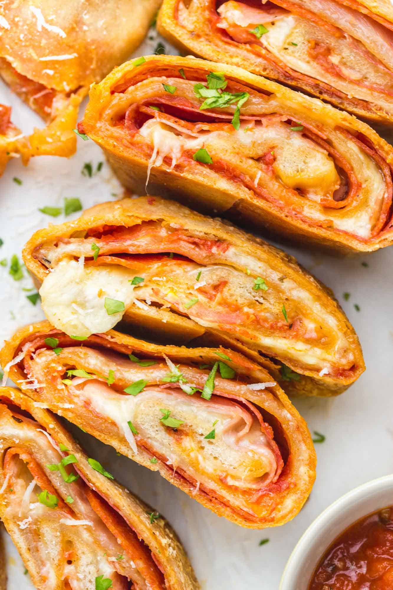 slices of stromboli filled with cheese and pepperoni on a plate, garnished with parsley and with a side of marinara sauce.