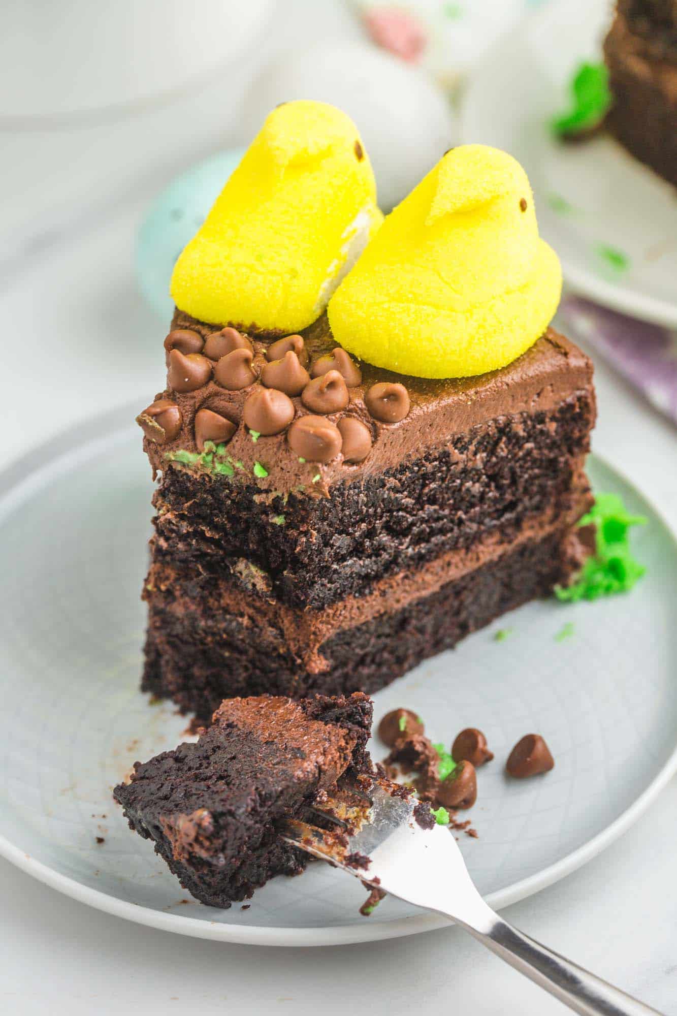 A slice of peeps sunflower chocolate cake on a plate. A fork has removed a bite from the front of the slice. 