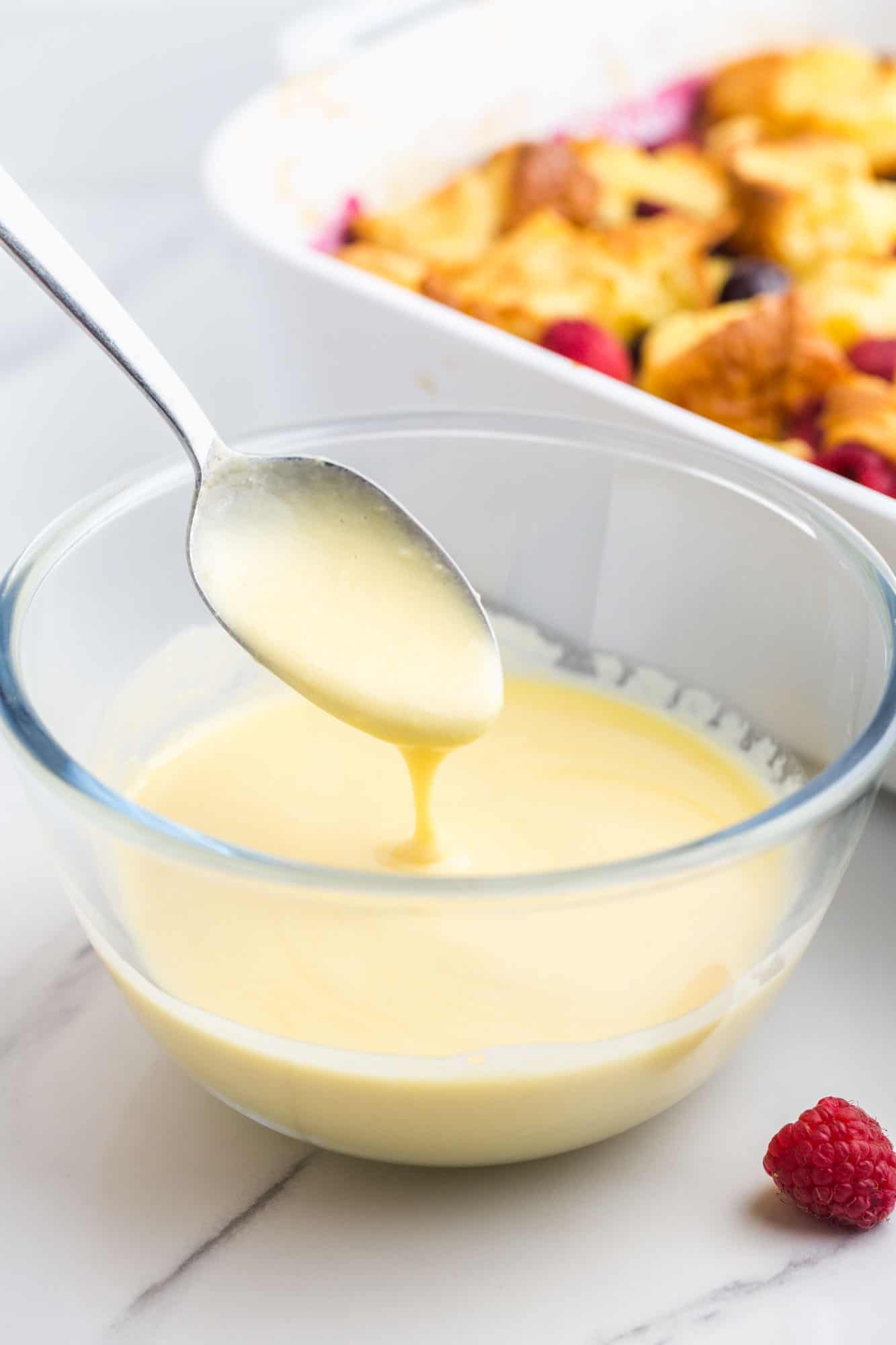 Simple vanilla sauce in a small glass bowl, and a spoon.
