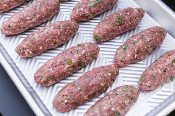 Raw beef kafta shaped into oblong patties on a metal baking sheet
