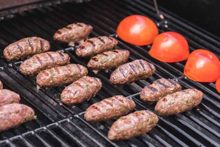 Beef kafta on the grill with tomato halves on the side
