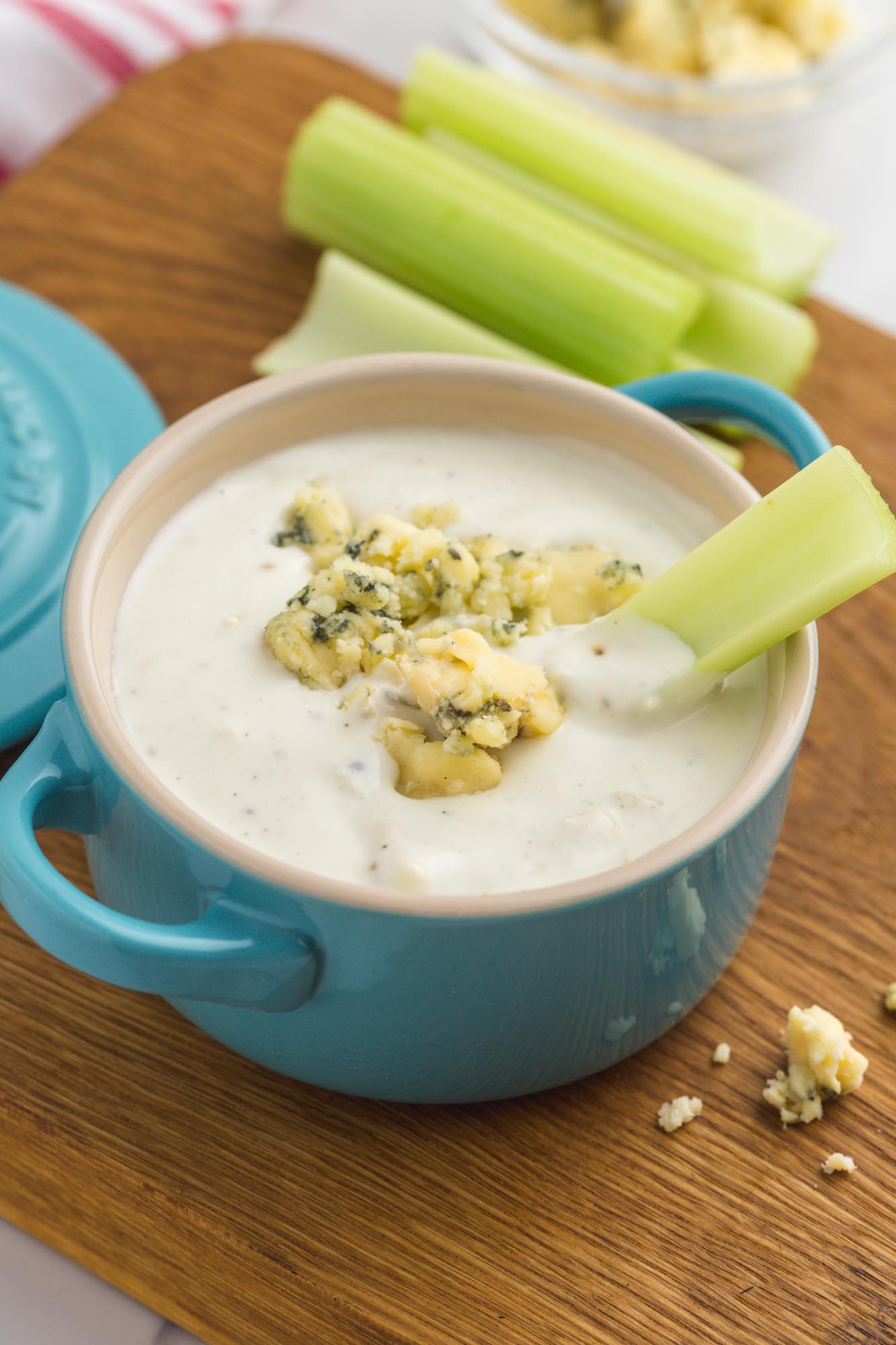 a blue crock filled with blue cheese dressing. a stack of celery sticks is in the background, and one celery stick is in the blue cheese.