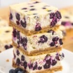 a stack of three blueberry cheesecake bars on a white plate.