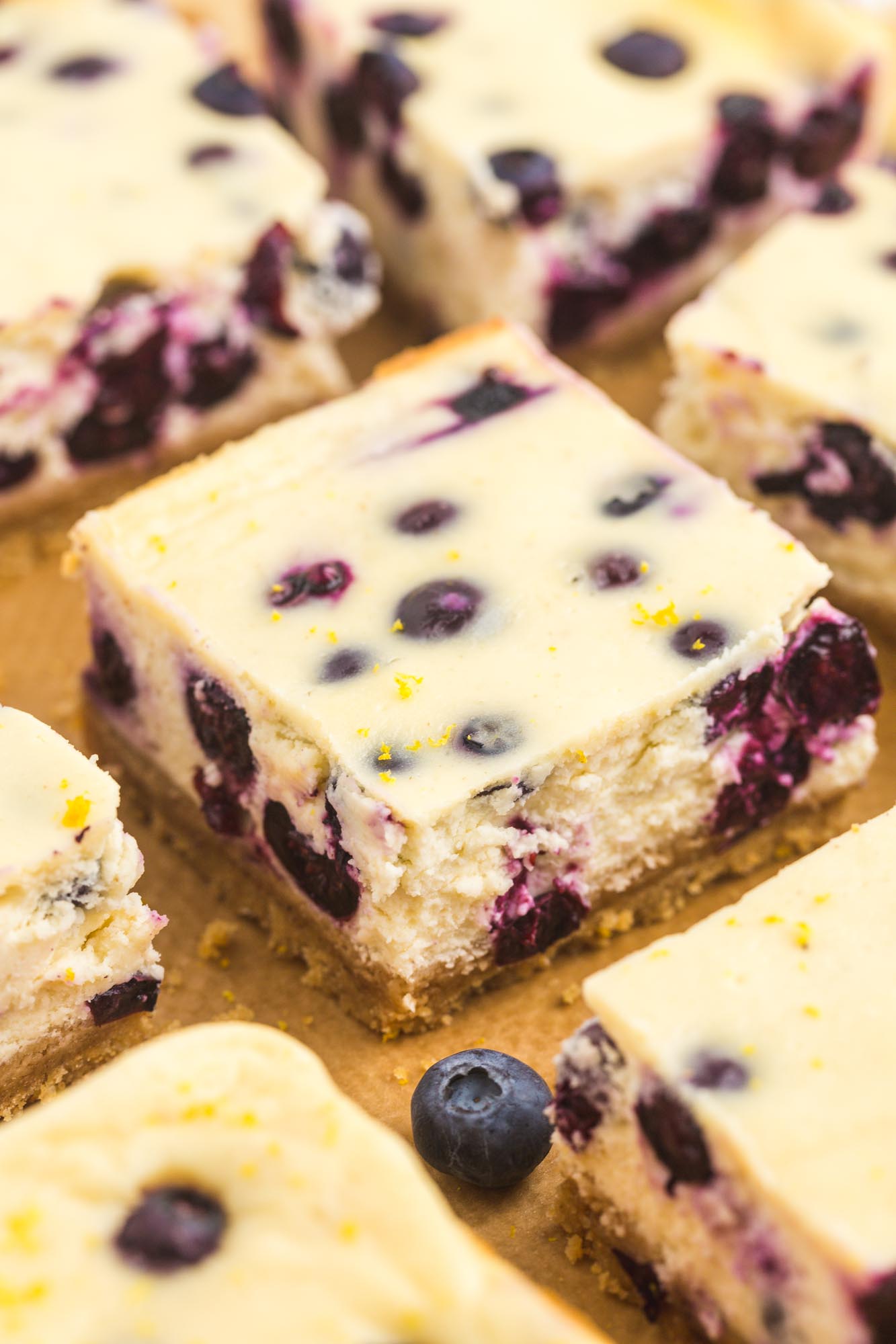 Blueberry cheesecake bars neatly lined up on top of a piece of undyed parchment, closeup image