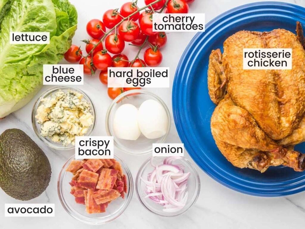 The ingredients for making a cobb salad, including a rotisserie chicken, eggs, bacon, and veggies all measured into separate bowls.
