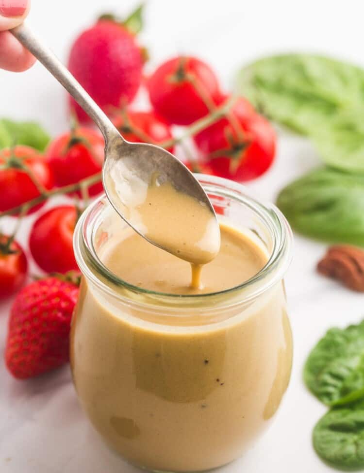 a small jar of creamy balsamic dressing on a talbe next to tomatoes, lettuce, berries and nuts.