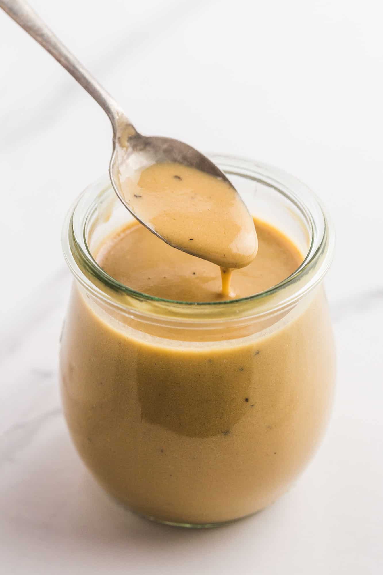 a small jar of creamy balsamic dressing being served with a teaspoon.