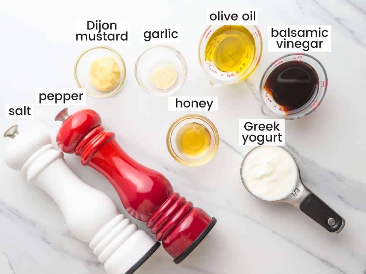 The ingredients for how to make creamy balsamic dressing, measured into small bowls next to red and white pepper and salt grinders