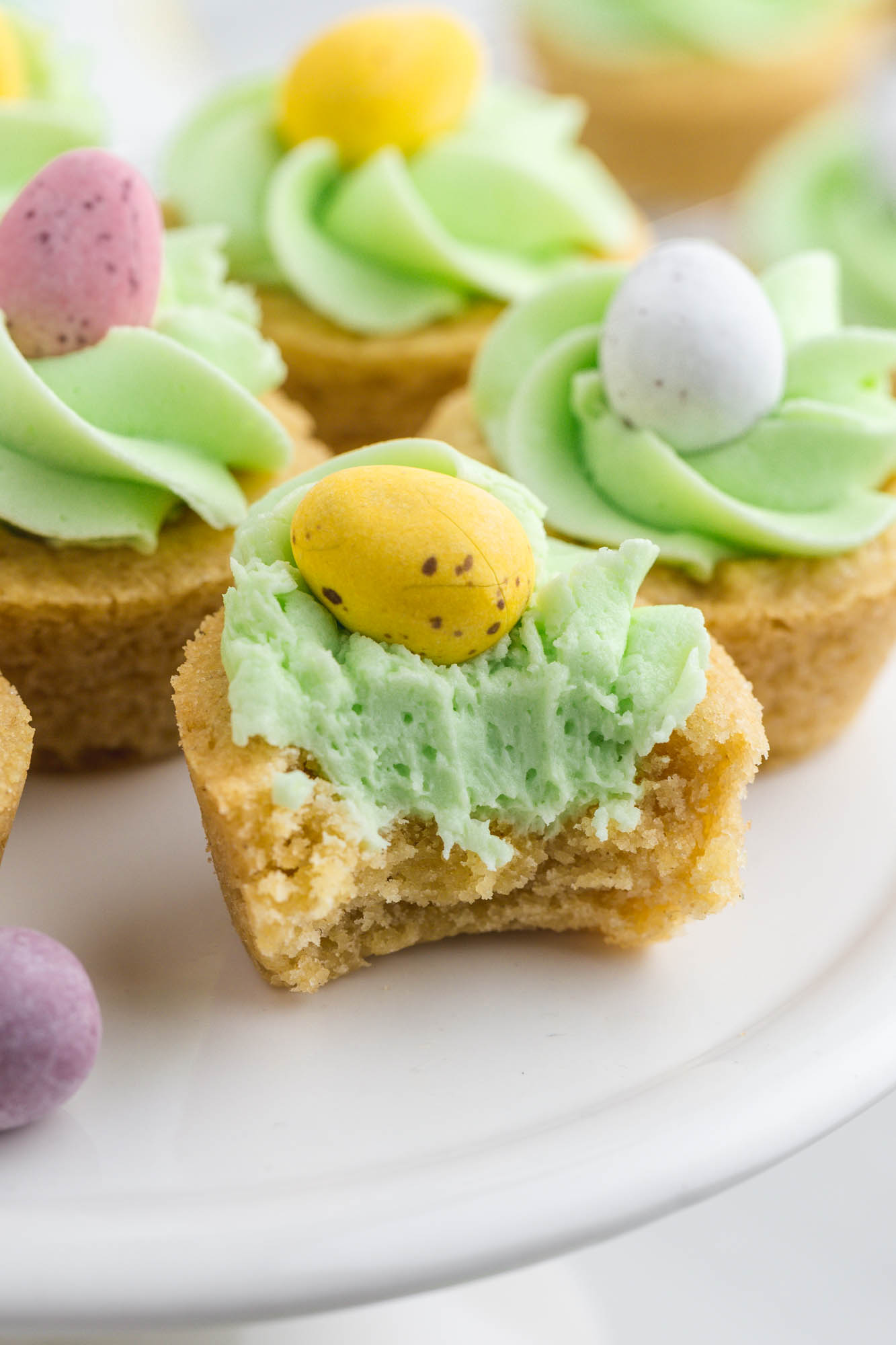 A bite shot of an easter basket cookie cup with light green buttercream frosting and chocolate mini eggs