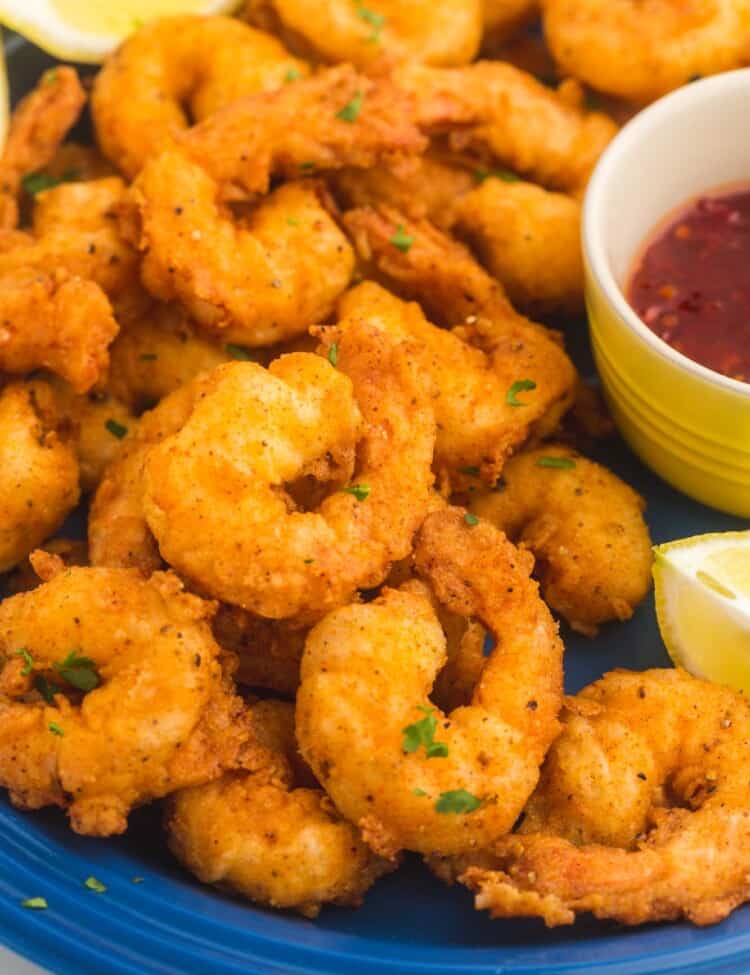 cropped image of a plate of fried crispy shrimp garnished with lemons and a side cup of red sauce