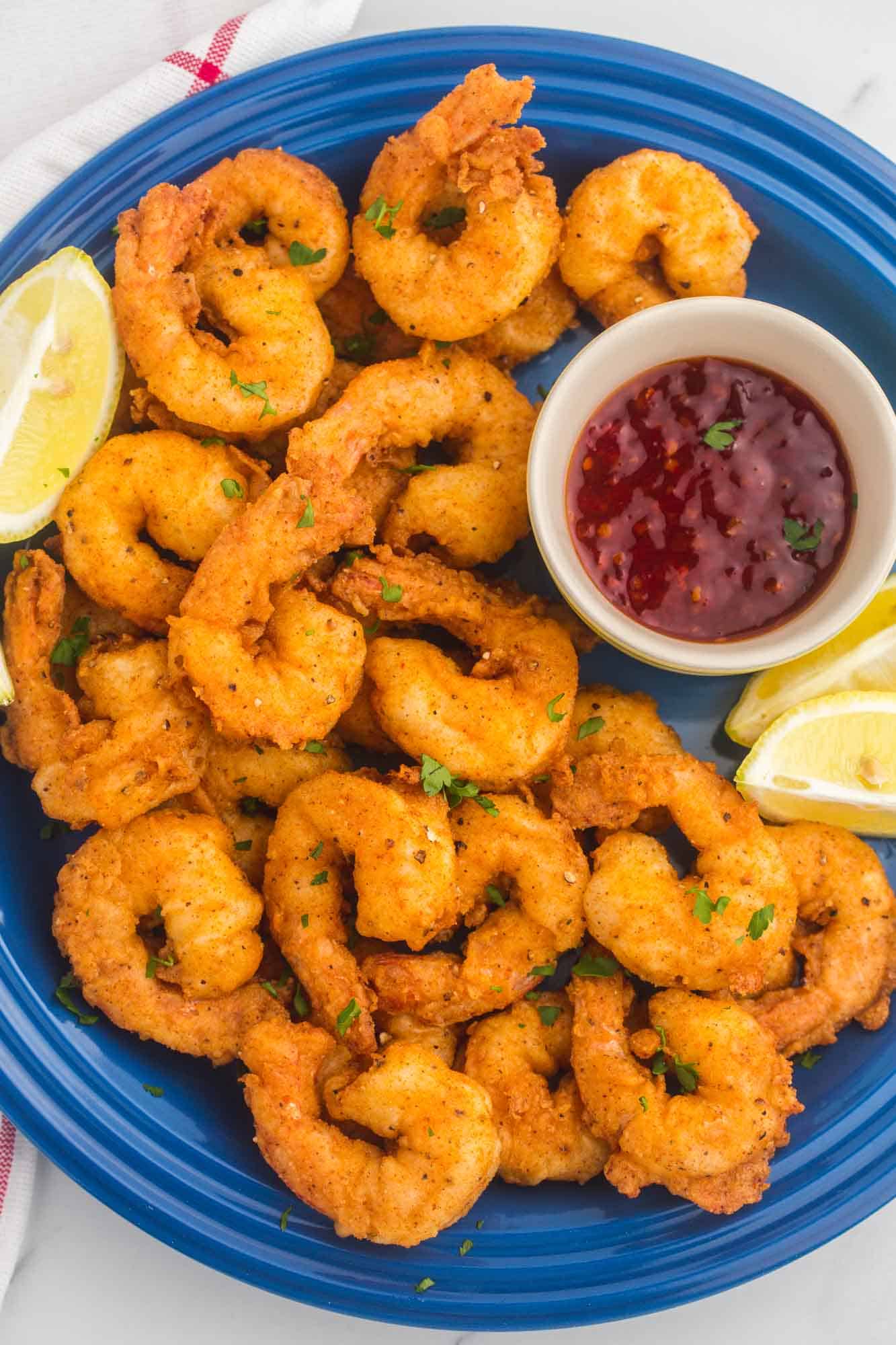 a large blue plate filled with fried shrimp. A cup of sweet chili sauce is on the side and the plate is garnished with lemon wedges