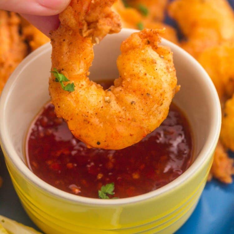 a large fried shrimp being dipped into sweet chili sauce that is in a yellow ramekin