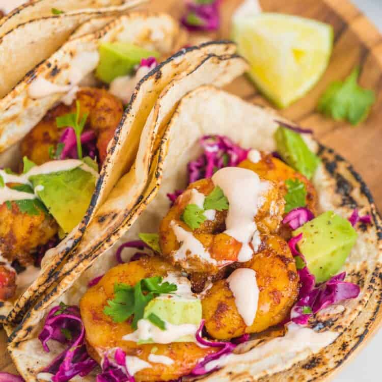Grilled shrimp tacos with avocado, creamy sauce, and fresh cilantro. Placed on a wooden tray.