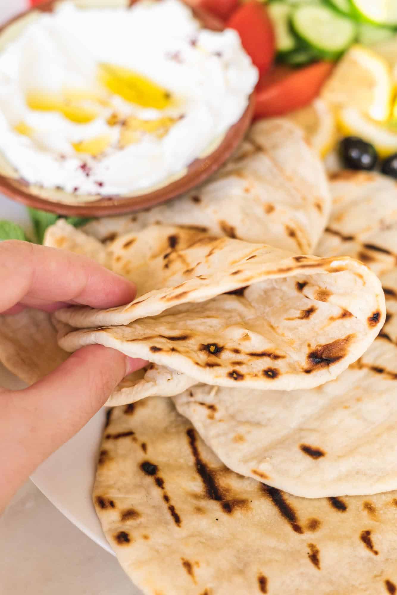 Holding a grilled flatbread to show that it's pliable and not brittle