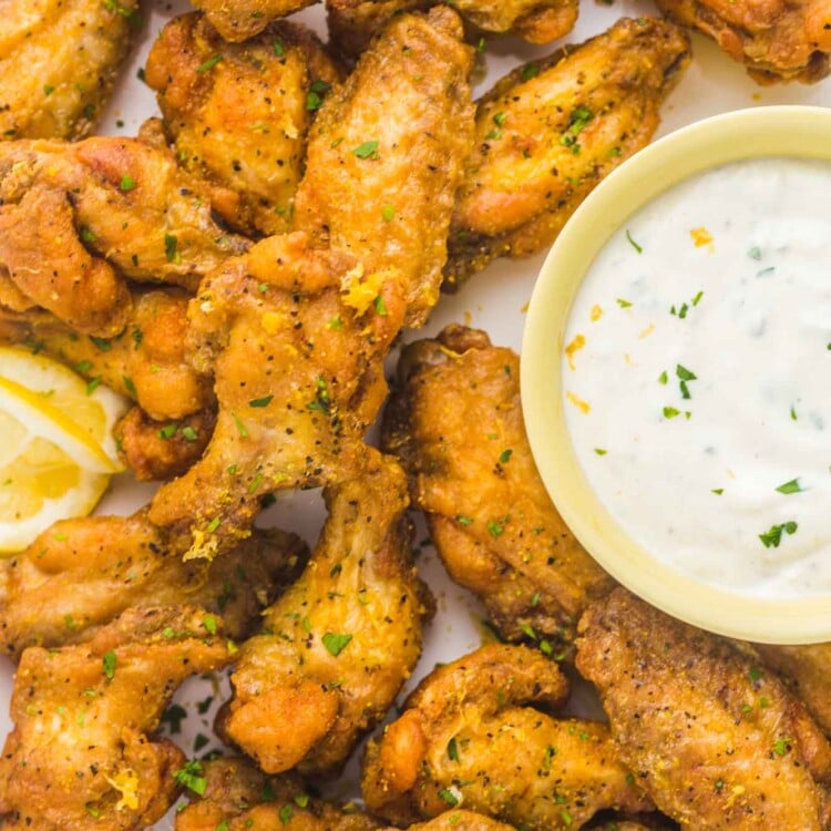 a plate of lemon pepper chicken wings with a side of blue cheese dressing in a small cup