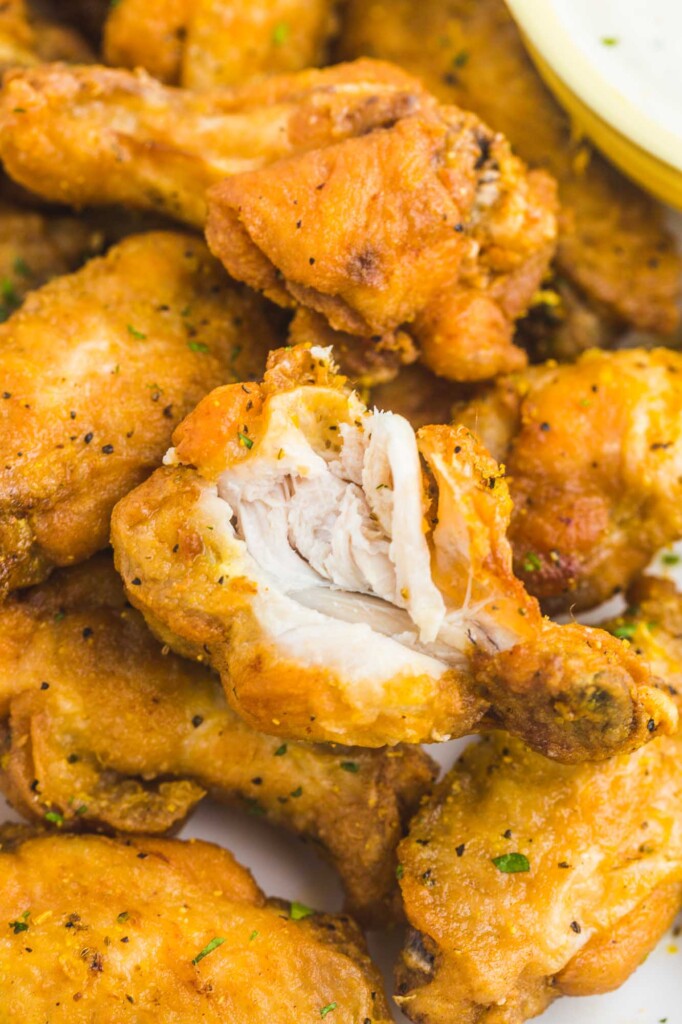 closeup shot of a plate of lemon pepper wings, a drumette has been bitten and set down to show the texture of the meat inside.