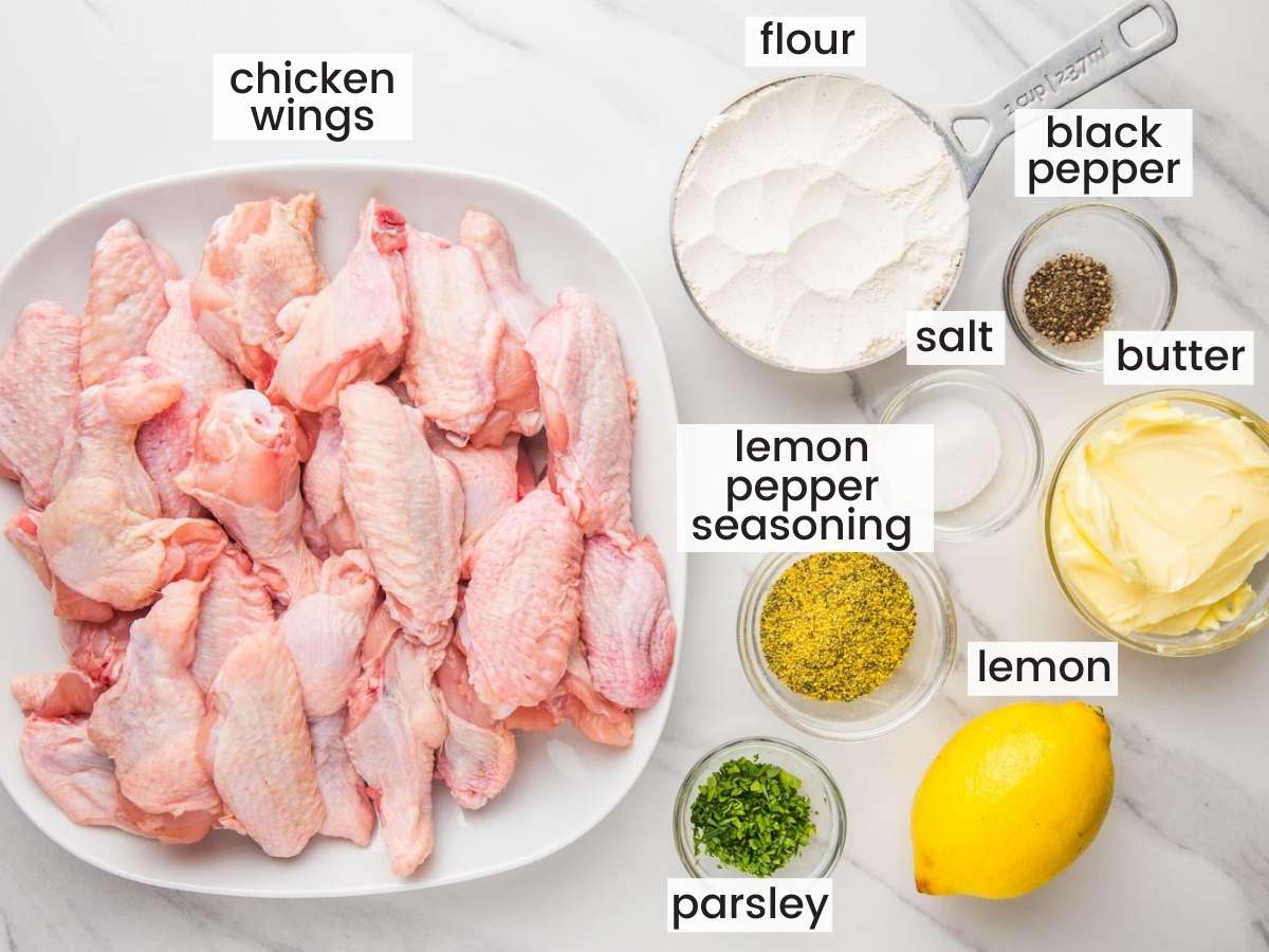 a plate of raw chicken wing pieces with the ingredients for cooking them with lemon pepper seasoning, all set out on a marble counter