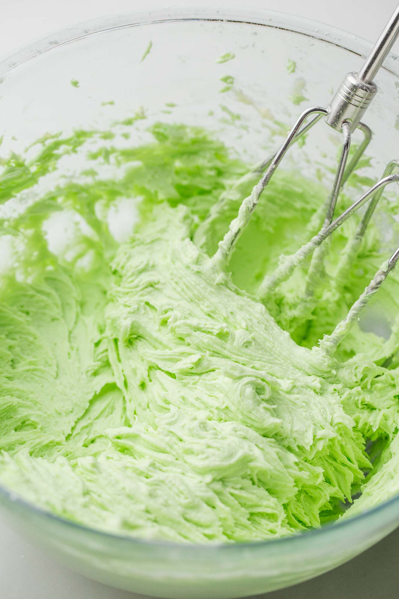 Light green whipped buttercream frosting in a large glass bowl