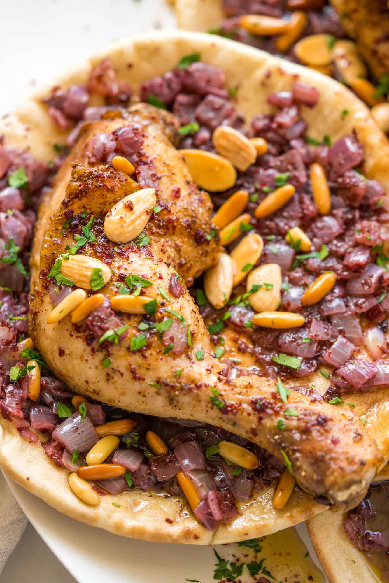 Close up shot of one musakhan flatbread with sumac onions, chicken, and toasted nuts.