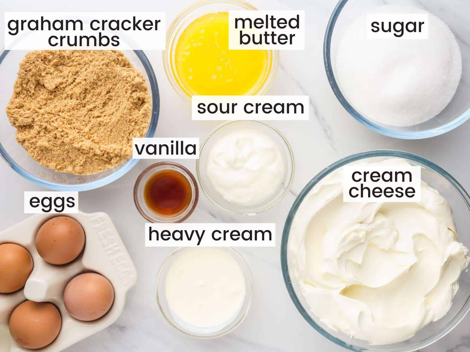 The ingredients needed to make a NY cheesecake from scratch, including cream cheese, sour cream and eggs. Measured into separate bowls, viewed from above. 